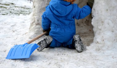 Kışlık tulumlu küçük bir çocuk karda mavi plastik bir kürekle yürüyor. Bir eskimo evi inşa edecek. Küçük çocuk buz mağarasına, deliğe, eve tırmanıyor. Eldivenleri ve tahta saplı küreği var..