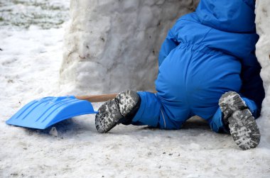 Kışlık tulumlu küçük bir çocuk karda mavi plastik bir kürekle yürüyor. Bir eskimo evi inşa edecek. Küçük çocuk buz mağarasına, deliğe, eve tırmanıyor. Eldivenleri ve tahta saplı küreği var..