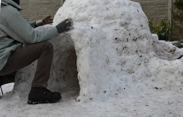 man, dad, builds a children's igloo house out of snow which is very little is dirty with grass clay. sticks snowballs and the house will be ready soon. children will have fun and a place to play