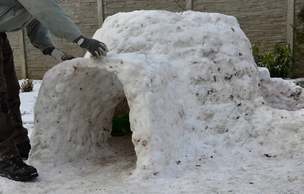 man, dad, builds a children\'s igloo house out of snow which is very little is dirty with grass clay. sticks snowballs and the house will be ready soon. children will have fun and a place to play