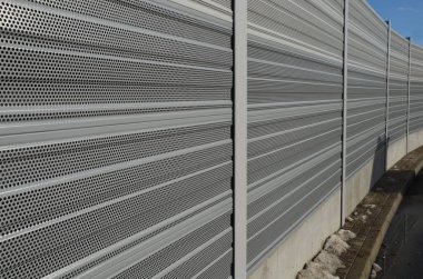 noise barrier made of metal perforated sheet metal slats. gray and silver protective fencing separates housing from a busy noisy road. the porous material shatters tire noise well clipart