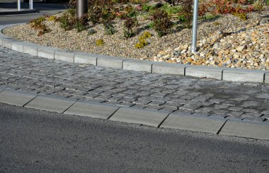 Merkeze yakın yuvarlanmış bir pervazda gri granit küplerin kaldırımları. eğimli beton kaldırımlar, bir ulaşım merkezi, çemberin ortasında çiçekler ve otlar var. çok yıllık çiçek tarhı 