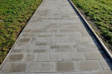 Kahverengi, gri beton park yolu, kaldırım kenarında. Farklı boyutlarda kiremitler birbirine uyuyor. Güneşin altında çimlerin etrafında. ön görünüm