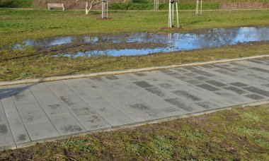 Parktaki su dolu toprak, bahar yağmurundan su almıyor. Yetersiz infaz edilmiş drenaj ya da çatlak otomatik sulama boru hattı bir sel yaratmış, yol kenarında bir trafik kazası.