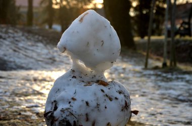 a snowman sadly slowly melting, dirty from mud and lack of snow will evoke a feeling of ruin and ugly changeable weather of winter February. frozen snow on lawn clipart