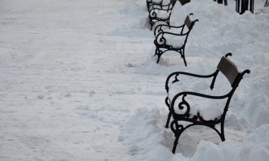 Metal bankların olduğu bir kare. Meydan karla kaplı ve traktörün kenara ittiği yığınları görebilirsiniz. Banklar büyük bir kar tabakasıyla kaplı. Kimse oturmuyor ve...