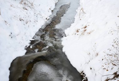 Donmuş akarsu, su açıkça görülebilir, ama buz yavaş yavaş onu kapatıyor. Derin bir vadideki soğuk, dondurucu su manzarası ve çağlayan küçük bir dere.