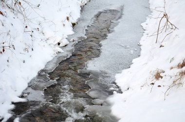 Donmuş akarsu, su açıkça görülebilir, ama buz yavaş yavaş onu kapatıyor. Derin bir vadideki soğuk, dondurucu su manzarası ve çağlayan küçük bir dere.