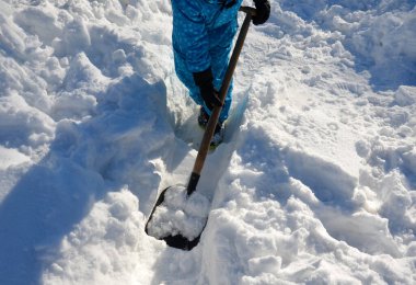 Çocuk evin etrafında bir kar felaketini temizlemeye çalışıyor. Elinde bir kürek, bir kürek tutuyor ve mavi bir tulumla karda çalışıyor..