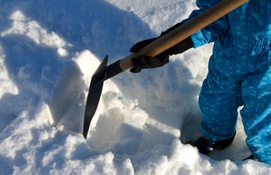 Çocuk evin etrafında bir kar felaketini temizlemeye çalışıyor. Elinde bir kürek, bir kürek tutuyor ve mavi bir tulumla karda çalışıyor..