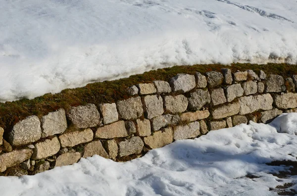retaining wall made of granite bricks by the road. the snow fit all around, only the wall remained visible in its beautiful texture of random cracks and crevices. construction art of drywall winter