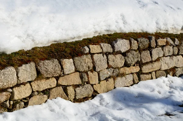 retaining wall made of granite bricks by the road. the snow fit all around, only the wall remained visible in its beautiful texture of random cracks and crevices. construction art of drywall winter