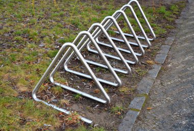 Parktaki meydanda turistler için bisiklet tekerleği saklamak için metal raflar. Yolun kenarına sabitlenmiş çeşitli şekillerde paslanmaz çelik borular, kaldırım kenarı fotoğrafı.