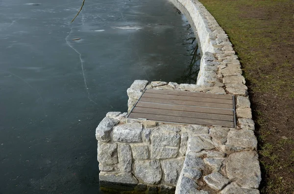 Stone retaining walls of a water reservoir or river pond dock, fortified granite walls. at the dam with a sluice for discharging water out into the stream. covered boards