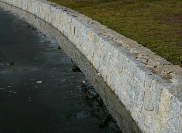 Stone retaining walls of a water reservoir or river pond dock, fortified granite walls. at the dam with a sluice for discharging water out into the stream. covered boards