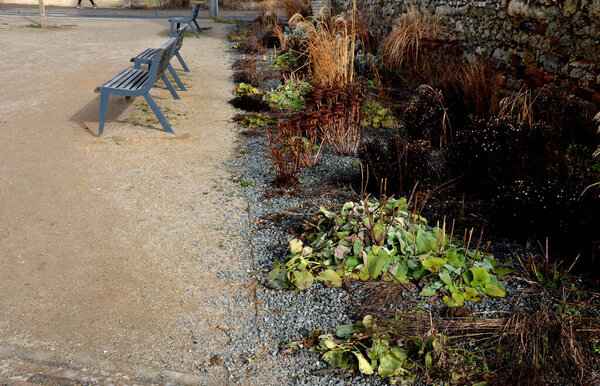 Perennial bed mulched with gray gravel in front of a limestone stone wall in a square with benches with wood paneling, beige path made of natural beige compacted crushed stone, park, urban garden stock photo