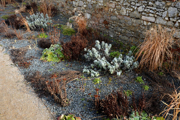 Perennial bed mulched with gray gravel in front of a limestone stone wall in a square with benches with wood paneling, beige path made of natural beige compacted crushed stone, park, urban garden stock photo