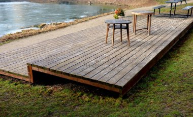 Su kenarında doğal ahşap sıralı ahşap banklar olan ahşap oturma alanı. Göletin yanındaki terasta piknik tezgahı ve kafe gibi yuvarlak masalar var. Liman iskelesi ördeklerle gölün yukarısına çıkıyor.