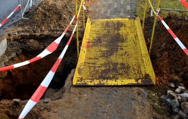 Kaldırımın yolu bir kablo kullanarak elektriği bağlamak için bir hendeğin kazılmasıyla kesilir. Yayalar ayaklarına zarar vermemek için dikkatli olmalı. Geçici köprü, sarı bir plaka fotoğrafı kullanıyor.