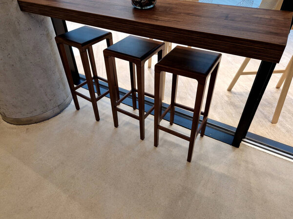 row ofsquare shaped bar chairs with backrest and a glass partition, suede upholstered dining table chairs. wooden table and floor in the cafe, brown