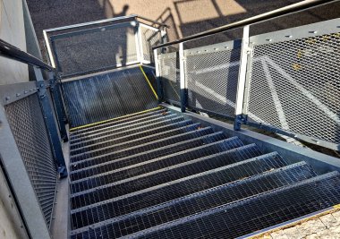 Endüstriyel salonda, ağır yüklenmiş çelik zemin ızgara ve parmaklıkların altında bile yüksek dirençle dolu dik bir merdivenin yan kapısı var. Genişletilmiş metal, güvenlik sarısının kenarları. 