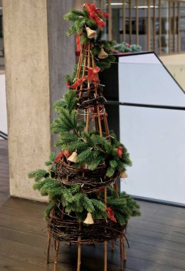 Dekoratif Noel ağacı koni şeklinde. Sarmaş dolaş söğüt hasırından ya da benzer doğal malzemeden yapılmış. Dallar yapıyı sarmalamışlar. Modern bir iç mekanda ahşap zeminde