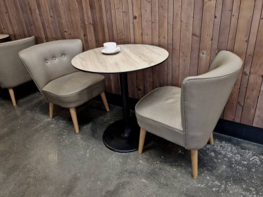 İki koltuğu ve oval masası olan bir kafe oturma alanı. Gri-kahverengi döşeme. Masanın ahşap bir üstü ve siyah dökme demiri var. Masanın üzerinde küçük beyaz bir kahve fincanı var. ahşap