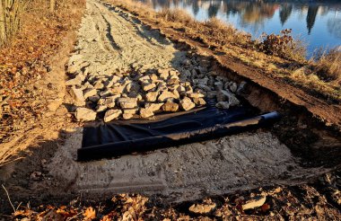 Kesişen yol inşa edilmiş ya da yeniden inşa edilmiş, muhtemelen bisiklet yolu, nehir boyunca patika. Asfaltsız ya da çakılsız bir yüzeyden yeni döşenmiş beton bir zemine geçiş. Etrafı beton kaldırımlarla çevrili. Bitmiş asfalt bölümü devam ediyor. Çevre