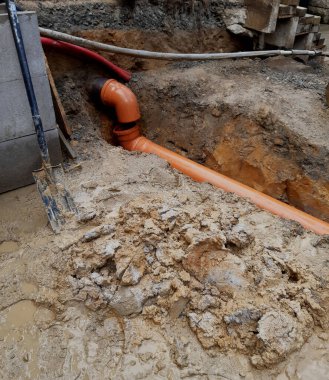 Turuncu plastik borular kullanarak bir açık hava kanalizasyon sisteminin kurulumu veya onarımı. PVC-U 'dan yapılmış kanalizasyon boruları, genellikle kanalizasyon şebekeleri ve indirme boruları için kullanılır. Boruların turuncu rengi standart tanımlamadır. İşçi yönetimi