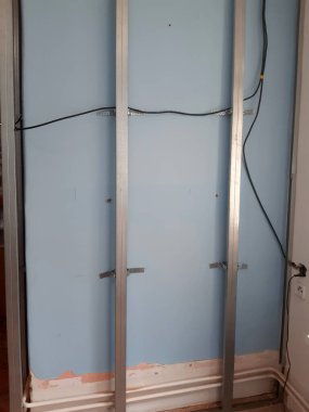 Alçıpanlı perde duvarı için metal şebeke yapısı. Dikey çelik profillerden yapılmış, ayarlanabilir akustik askılar kullanılarak duvara tutturulmuş kıvrımlı duvarlar, kablolar için kurulum boşlukları oluşturulması, termal gürültü yalıtımı geliştirilmesi.