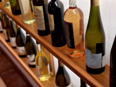 Ahşap raflarda sergilenen şarap şişeleri. Bu, beyaz, gül ve kırmızı dahil olmak üzere farklı türde şarap koleksiyonudur. Şişelerin şekil ve boyutları farklı. LED şeritli arka ışıklandırma