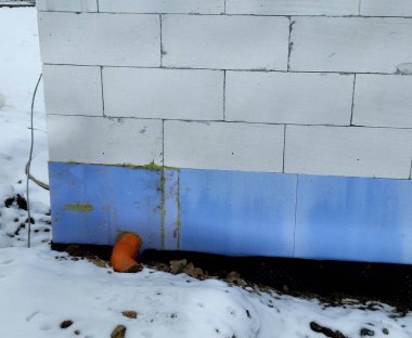 Yeraltı katının çevresinde polistiren plakalar olan termal yalıtım. Kaynamış folyoyla suya ve neme karşı izolasyon. Binanın etrafını doldur. Toprak serpme temeli