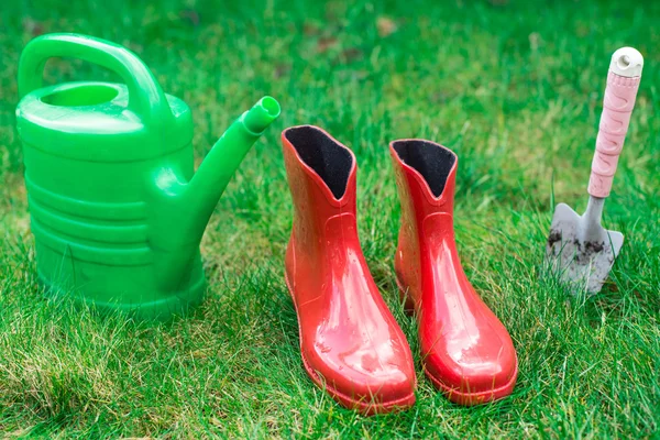 Садовые инструменты, красные садовые ботинки, маленькая лопата, лейка на траве, крупным планом . — стоковое фото