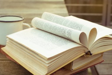 Ahşap masa Vintage Kitap eski moda bardak çay ile açıldı. Kalp şeklinde sayfa. Yan görünüm.