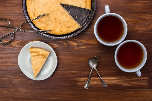 Nowojorski sernik na rustykalne drewniane tła z filiżanką herbaty, kleszcze na deser. — Zdjęcie stockowe