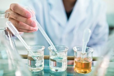 Kimyasal laboratuvar, kimyasal şişeler taşıyan personel ve deney şişesine bakan....