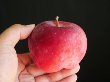 Kırmızı elma tutan bir el, siyah arka plan.