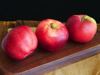 Üç kırmızı elma, koyu arkaplan, meyveleri yakın plan.