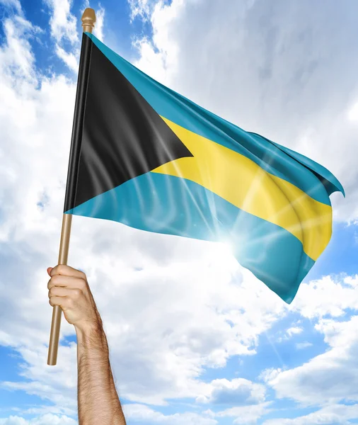 มือของบุคคลที่ถือธงชาติบาฮามาส และโบกมันบนท้องฟ้า — ภาพถ่ายสต็อก