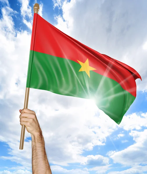 Mano de la persona sosteniendo la bandera nacional de Burkina Faso y agitándola en el cielo, parte 3D representación —  Fotos de Stock