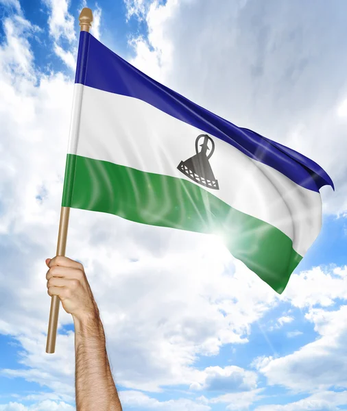 Person 's hand holding the Lesotho national flag and waving it in the sky, 3D rendering — стоковое фото