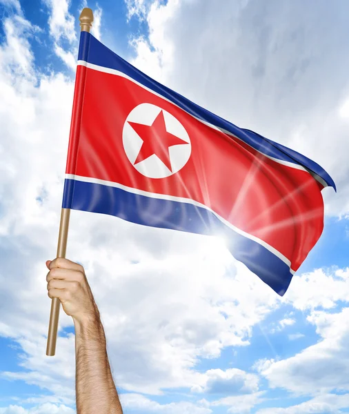 Mano de la persona sosteniendo la bandera nacional de Corea del Norte y agitándola en el cielo, representación 3D —  Fotos de Stock