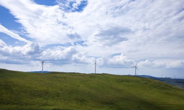 Dağdaki rüzgar türbinleri mavi gökyüzünün altında.