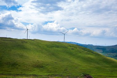 Dağdaki rüzgar türbinleri mavi gökyüzünün altında.