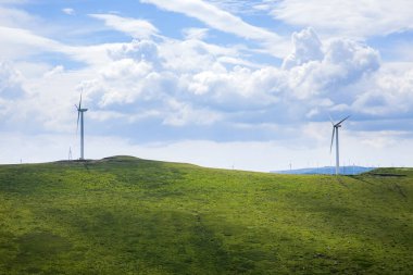 Dağdaki rüzgar türbinleri mavi gökyüzünün altında.