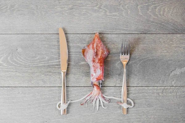 Färsk bläckfisk på träbord med gaffel och kniv — Stockfoto