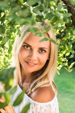Sarışın bir genç güzel kadın ile parlak yeşil ağaç altında bırakır