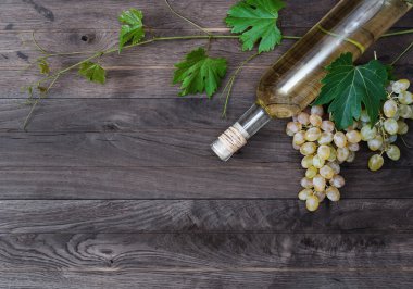 Bir şişe beyaz şarap ve ahşap zemin üzerine taze üzüm