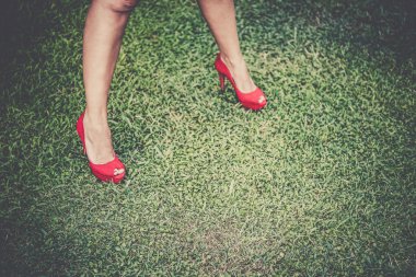 Kadının bacaklarını açıp çimenlerin üzerinde yüksek topuklu parlak kırmızı ayakkabılar