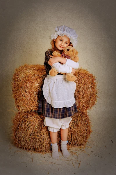 Menina abraçando um urso perto do feno . — Fotografia de Stock